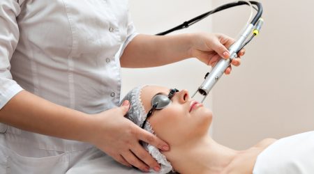 Woman lying on a table with protect glasses on eyes getting a laser skin treatment in healthy beauty spa salon